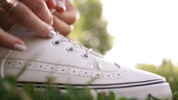 Close up view of female runners hands with wedding ring ties up her shoelaces on white sneakers on green grass on a morning run — Stock Video