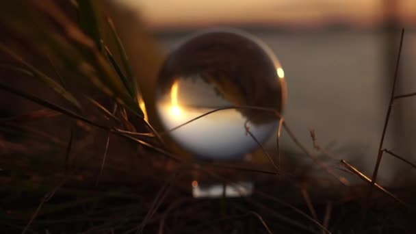 草の中の夕日の光の中でガラス玉が風に揺れる。全世界を反映しています。ライフスタイル・ショット。広告映画撮影。運命、未来、過去、現在。旅行. — ストック動画