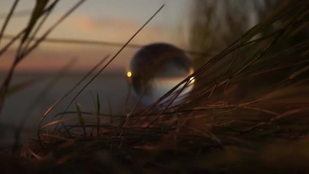 Скляний м'яч у променях заходу сонця в траві різко махає вітром. відображення всього світу. життєвий постріл. рекламний кінематографічний знімок. Доля, майбутнє, минуле, сьогодення. Подорожі . — стокове відео
