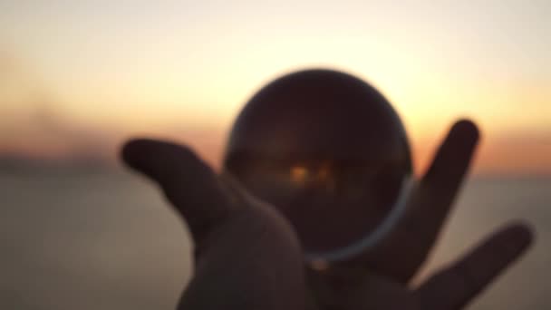 Main masculine tient une boule de verre sur un fond de coucher de soleil en mer. Tournage cinématographique dramatique. Silhouette .