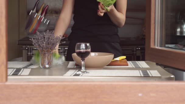 Mujer joven cocinando en la cocina haciendo la cena Almuerzo preparando pausas para comer Lechuga, lavanda, una copa de vino, a través de una ventana una casa privada — Vídeo de stock