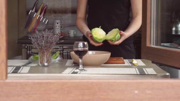 Mujer joven cocinando en la cocina haciendo la cena Almuerzo preparando pausas para comer Lechuga, lavanda, una copa de vino, a través de una ventana una casa privada — Vídeos de Stock