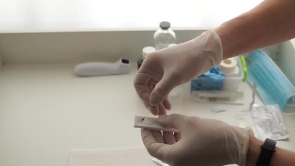 De artsen geven witte handschoenen af en druppelen een druppel bloed op een snelle coronavirustest. Bloeddruppelaar — Stockvideo