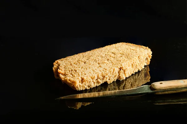 A slice of brown bread and a knife  on a black glass — Stock Photo, Image