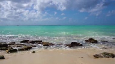 Waves crash on large stones lying on the sandy shore of the Caribbean Sea