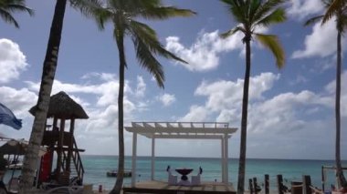 Served table prepared for newlyweds on a wooden deck under palm trees against a sunny sky with white clouds