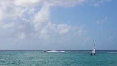Scooter swept along the sea waves at high speed past a small boat under sail