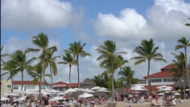 Rest in the hotel around the pool under umbrellas against the blue sky with white clouds