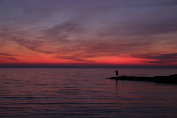 silhouette of a fisherman at sunset or sunrise. Bright colors of the sunset. Red sunset.