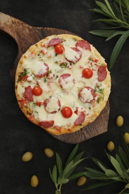 Mozzarella peynirli biberli pizza, sosis salam, baharat, domates, zeytin ve süsleme için zeytin dalı. İtalyan pizzası siyah arka planda izole edilmiş. Yemek arkaplanı. Düz yerde, üst tarafta. Restoran için fotoğraf menüsü.