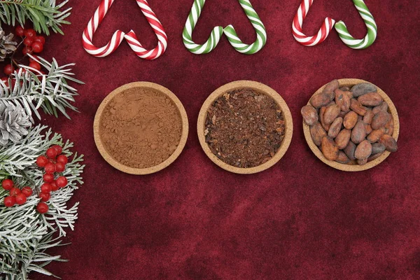 organic cacao beans, cocoa powder, ground and chocolate with caramel candy canes and branch of spruce on a red background. Vegan food. Flat lay. Top view. Christmas background, pattern, card, menu