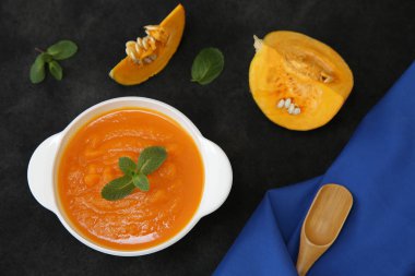 Siyah bir arka planda, kaşık, fesleğen, balkabağı dilimi ve metin veya görüntü için yeri olan kumaş peçeteli bir kasede kabak çorbası püresi. Diyet, menü, yemek geçmişi, kart. Sağlıklı gıda konsepti. Üst Manzara. Düz yatıyordu.