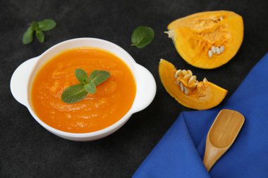 Siyah bir arka planda, kaşık, fesleğen, balkabağı dilimi ve metin veya görüntü için yeri olan kumaş peçeteli bir kasede kabak çorbası püresi. Diyet, menü, yemek geçmişi, kart. Sağlıklı gıda konsepti. Üst Manzara. Düz yatıyordu.