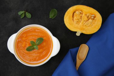 Siyah bir arka planda, kaşık, fesleğen, balkabağı dilimi ve metin veya görüntü için yeri olan kumaş peçeteli bir kasede kabak çorbası püresi. Diyet, menü, yemek geçmişi, kart. Sağlıklı gıda konsepti. Üst Manzara. Düz yatıyordu.