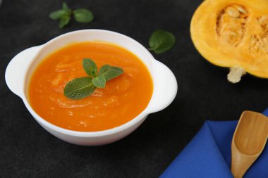 Siyah bir arka planda, kaşık, fesleğen, balkabağı dilimi ve metin veya görüntü için yeri olan kumaş peçeteli bir kasede kabak çorbası püresi. Diyet, menü, yemek geçmişi, kart. Sağlıklı gıda konsepti. Üst görünüm.