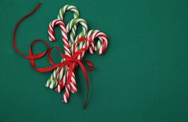 Yeşil arka planda kırmızı kurdeleyle bağlanmış şeker kamışları. Noel arkaplanı. Noel ve Yeni Yıl kavramı. Karamel şeker kamışı kavramı uzayı taklit eder. Düz yatıyordu. Desen, kart, çerçeve.