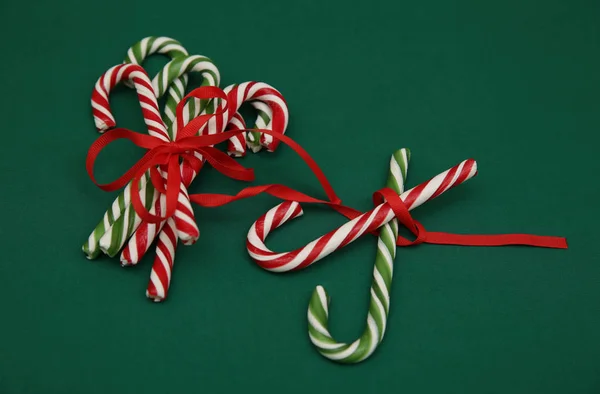 Pile Candy sugar canes tied with a red ribbon on a green background. Christmas background. Concept of Christmas and New Year. Caramel sugar cane concept Copy space. Close-up. Pattern, card, frame.