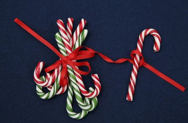 Pile Candy sugar canes tied with a red ribbon on a blue background. Christmas background. Concept of Christmas and New Year. Caramel sugar cane concept Copy space. Close-up. Pattern, card, frame.