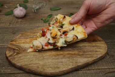 El, ahşap bir kırsal masada, üzerinde midye ve mozzarella peyniri olan bir dilim deniz ürünleri pizzası tutuyor. Akdeniz yemekleri. Vejetaryen. Metin için kopyalama alanı ile.
