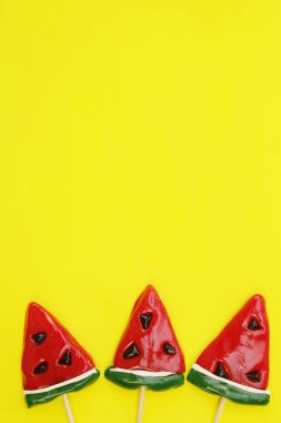 Sarı arka planda izole edilmiş karpuz şeklinde lolipoplar. Şekerleme arka planı. Tatil ve hediye kavramı. Üst Manzara. Düz yatıyordu. Metin için kopyalama alanı ile.