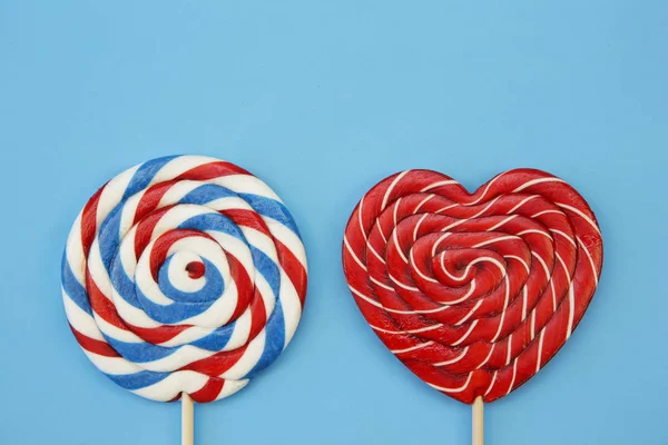 lollipops in the form of a red heart and a red-blue-white spiral isolated on a blue background. Confectionery. The concept of holidays and gifts. With copy space for text.