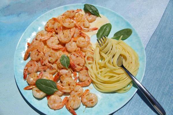 Flat lay Italian pasta with shrimps in sauce on the blue plate and background. Top view.
