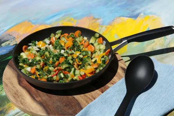 vegetable ratatouille of colored vegetables in a pan, on a wooden board and a colored background with a spoon. Vegetarian food concept. Copy space for text.