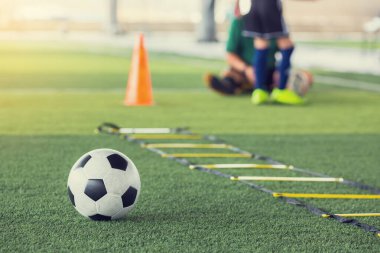 Yeşil yapay çimenlikte bulanık futbol topu ve merdiven matkapları.
