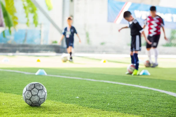 Pallone da calcio su tappeto erboso artificiale verde con squadra di calcio sfocata tra — Foto Stock