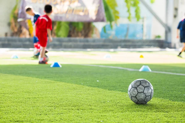 Pallone da calcio su tappeto erboso artificiale verde con squadra di calcio sfocata tra — Foto Stock