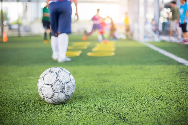 Pallone da calcio sul tappeto erboso artificiale verde con gioco di calcio bambino sfocato — Foto Stock