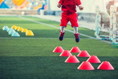 Çocuk futbolcu G 'deki kırmızı koni işaretleri arasında koşuyor ve zıplıyor