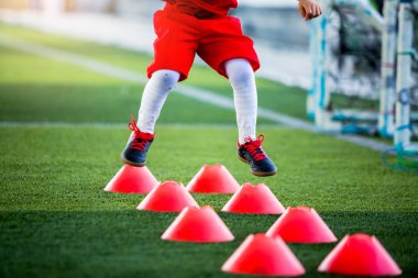 Çocuk futbolcu G 'deki kırmızı koni işaretleri arasında koşuyor ve zıplıyor