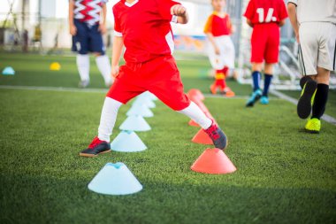 Çocuk futbolcu kırmızı ve mavi koni markası arasında koşuyor ve zıplıyor