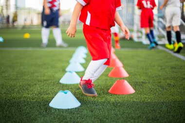 Çocuk futbolcu kırmızı ve mavi koni markası arasında koşuyor ve zıplıyor