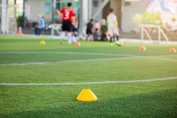 マーカーコーン上の緑の人工芝とともにぼやけた子供のサッカーのプレー — ストック写真