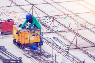 İnşaat işçisi ve inşaat alanında elektrikli demir bükme makinesiyle çalışan deforme olmuş pek çok çelik çubuk. Büyük ölçekli yüksek ölçekli inşaat projesi.