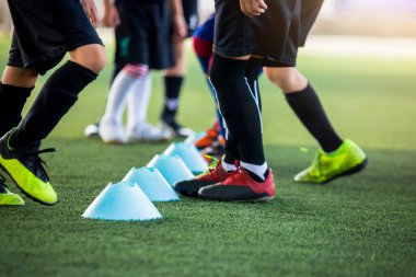 Çocuk futbol oyuncuları için seçici bir odak noktası, futbol antrenmanı için yeşil suni sahada koni işaretleri arasında koşuyor ve atlıyor. Futbol ya da Futbol Akademisi.