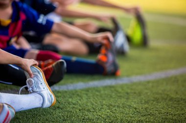 Spor geçmişi için bulanık bir görüntü. Çocuk futbolcular ayaklarını yakalamak için ellerini uzatıyor. Yarışmadan önce vücut ve ayakları ısıtmak ya da alıştırma yapmak.