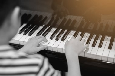 Siyah beyaz görüntü. Piyano çalmak için çocuk parmaklarına ve piyano tuşuna özen göster. Konser için müzik aleti ya da öğrenme müziği var. Sahnede piyano çalan çocuk müzisyenin eli kapalı.