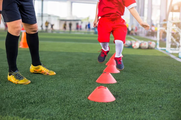 Kid soccer jogging and jump between cone marker with coach standing to coaching in soccer academy. Coach is coaching kid soccer player to jogging and jump between ladder drills for exercises.