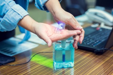 Coronavirus Covid-19 'un bulaşmasını önlemek için alkol dezenfektanı ile el yıkamak. Bulanık dizüstü bilgisayarla el yıkama ve ofiste telefon. Covid 19 'u korumak için ofisteki temizlik kavramı.