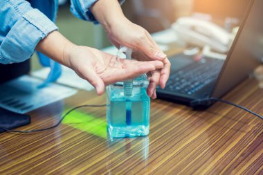 Coronavirus Covid-19 'un bulaşmasını önlemek için alkol dezenfektanı ile el yıkamak. Bulanık dizüstü bilgisayarla el yıkama ve ofiste telefon. Covid 19 'u korumak için ofisteki temizlik kavramı.