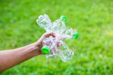 Bir adam elinde çimenlerin yeşil arka planında boş bir plastik şişe sıkıyor. Plastik problem ve başarısızlık ya da imha ve geri dönüşüm. Plastik kirliliğini durdurma kavramı, küresel ısınma.