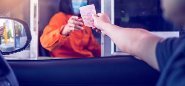 Sürücüye odaklanmak, kadın personele ekspres yol için ödeme yapmak Coronavirus Covid-19 ve Başbakan 2.5 tozunu korumak için maske takmak. Adam otoyol gişesi girişi için kasiyere para ödüyor..