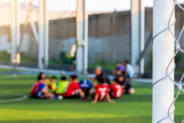 Beyaz kafes amacı ile koç ile yeşil yapay çim üzerinde oturan bulanık genç çocuk futbol oyuncuları.