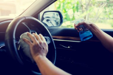 Şoförün eli Coronavirus Covid19 'u öldürmek ya da mikrop bulaştırmak için direksiyona alkol sıkıyor. Sürücü sık sık alkol püskürten yerleri temizleyip siliyor..