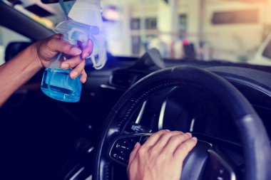 Şoförün eli Coronavirus Covid19 'u öldürmek ya da mikrop bulaştırmak için direksiyona alkol sıkıyor. Sürücü sık sık alkol püskürten yerleri temizleyip siliyor..