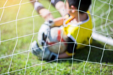 Kalecinin elinde top bulanıklığı, kalede yeşil çimlerin üzerinde. Kaleci topu yakalıyor. Asyalı futbolcu çocuk. Akademide futbol eğitimi. Spor bulanık arkaplan.