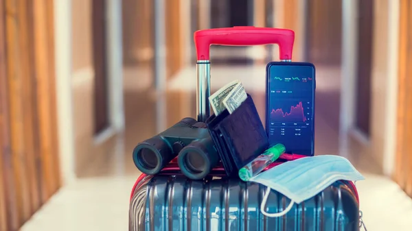 医療用マスク ドル札 双眼鏡やホテル内の荷物の上の旅行機器とスマートフォン上の赤いグラフ 経済の概念はコヴィト19世からのものである 旅行業の低迷 — ストック写真